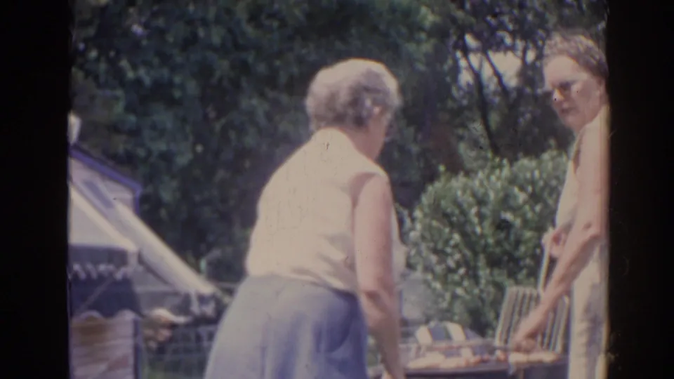 1962 Florida backyard scene with two older women beside a barbecue grill, one turned away and one partly facing the camera.