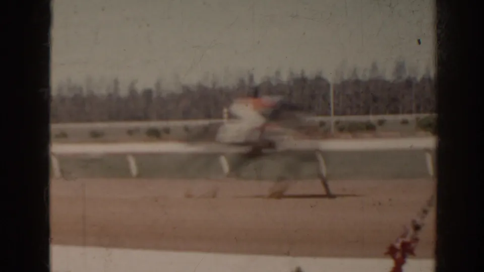 1962 Florida home-movie frame showing a blurred horse and rider moving along a racetrack with white rails.
