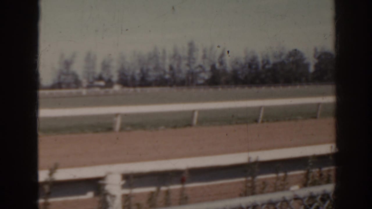 1962 Florida 8mm frame with the empty dirt track, white railings, distant treeline, and visible contact-sheet frame division.