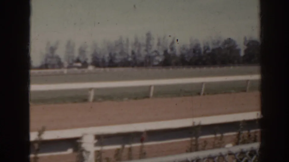 1962 Florida 8mm frame with the empty dirt track, white railings, distant treeline, and visible contact-sheet frame division.