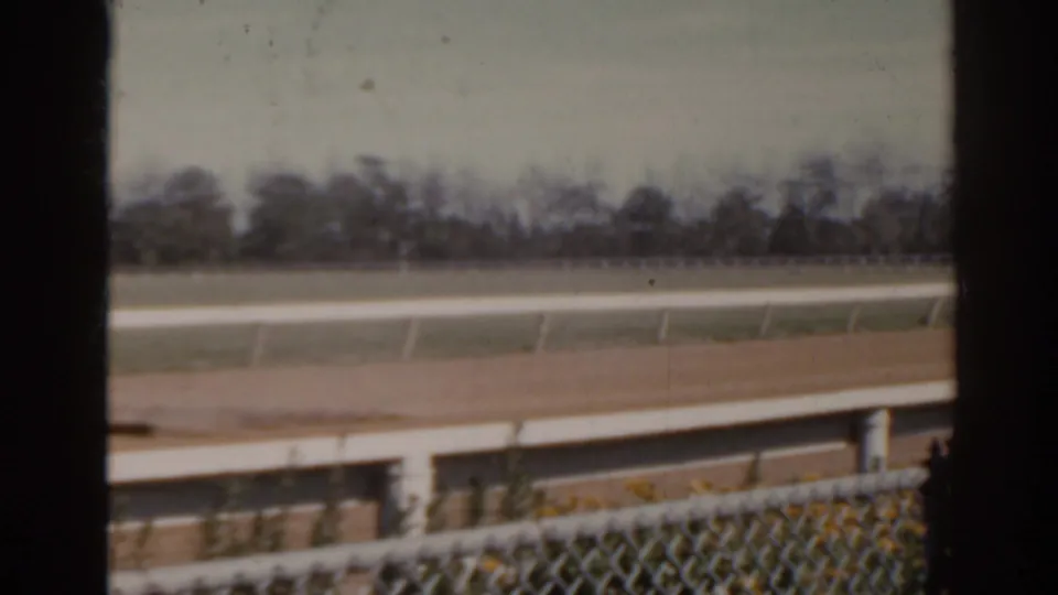 1962 Florida racetrack view with the tractor mostly out of frame, showing railings, fencing, dirt track, and distant trees.