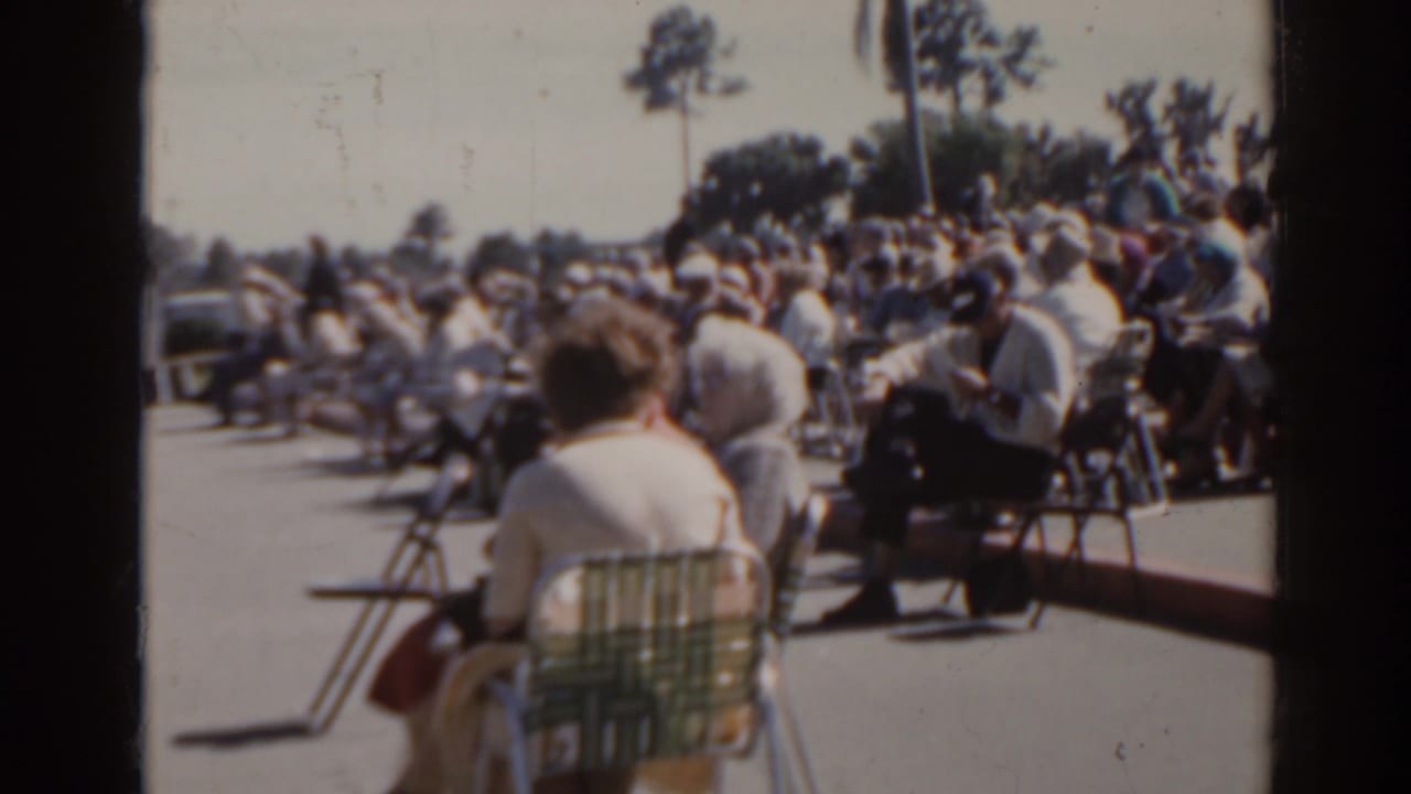 1962 Florida spectator scene at a local racetrack, with adults seated in folding chairs and vehicles visible behind the crowd.