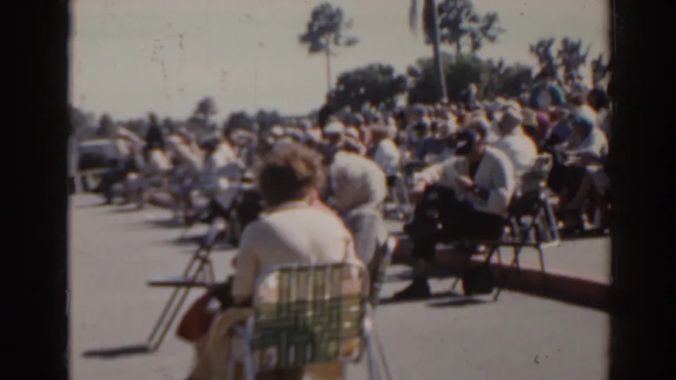 1962 Florida spectator scene at a local racetrack, with adults seated in folding chairs and vehicles visible behind the crowd.