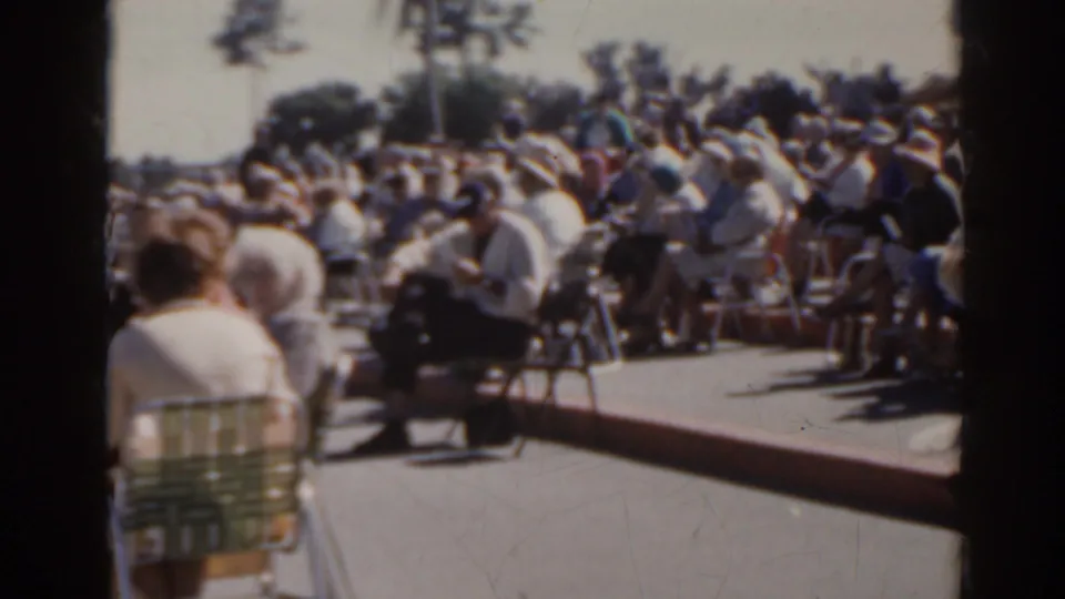 Seated spectators fill the frame in 1962 Florida outdoor-event footage, with palm trees beyond the crowd.