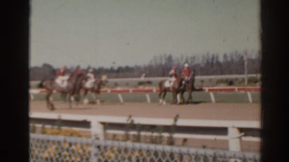 1962 Florida home-movie frame showing horses and riders on a dirt racetrack with spectators out of frame.