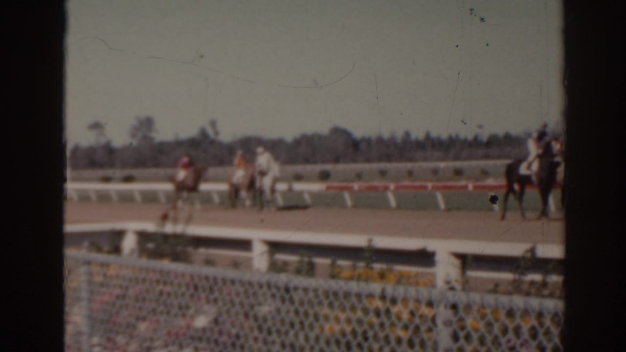 1962 Florida 8mm frame with a horse and rider partly at the right edge and other riders farther along the racetrack.