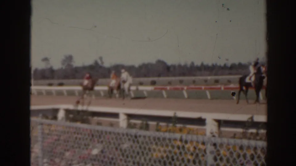 1962 Florida 8mm frame with a horse and rider partly at the right edge and other riders farther along the racetrack.