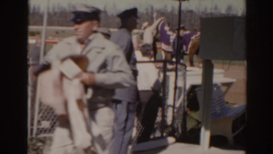 1962 Florida racetrack view of a uniformed attendant passing close to camera with horses and spectators behind him.