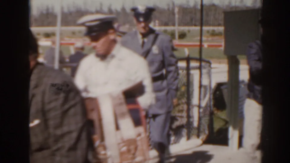 1962 Florida racetrack scene with uniformed officials and a man in a light shirt moving near the trackside gate area.