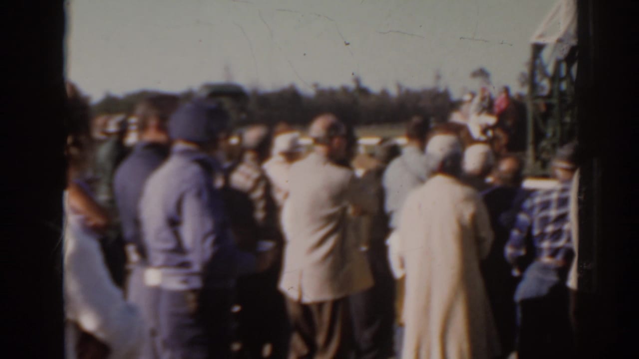 Crowd members watch from the rail at Sunshine Park racetrack, with the starting gate partly visible at frame right.