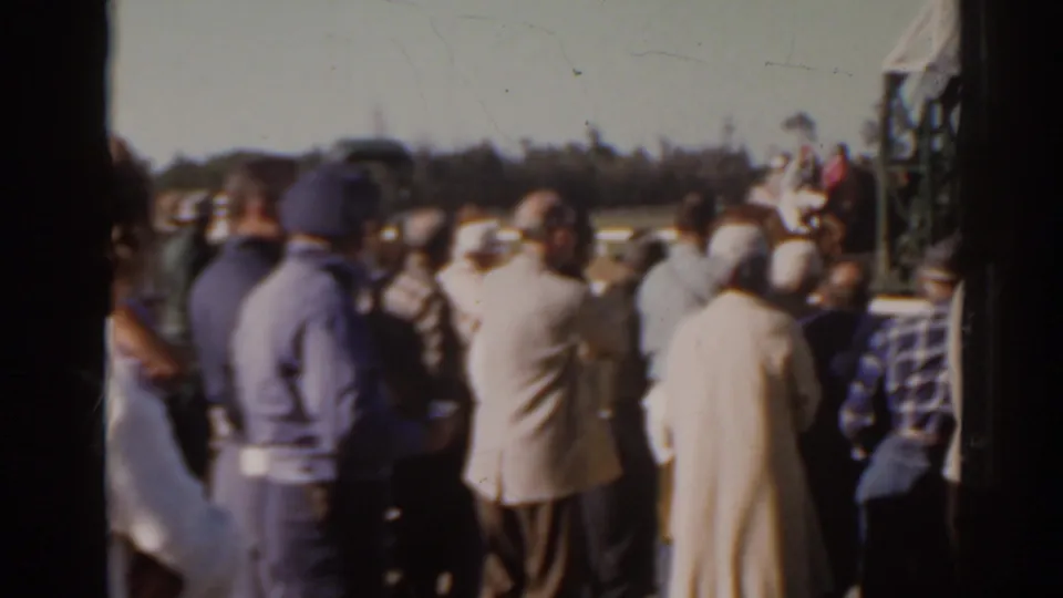 Crowd members watch from the rail at Sunshine Park racetrack, with the starting gate partly visible at frame right.