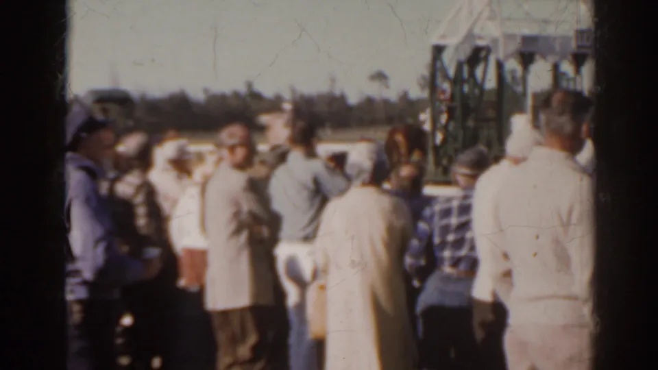 1962 Florida home-movie frame showing spectators from behind near a racetrack as starting gates stand beyond the rail.