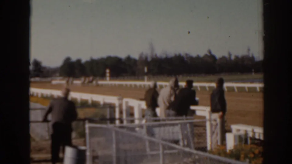 Spectators at a Florida racetrack in 1962 stand behind white rail fencing while the dirt track extends into the distance.