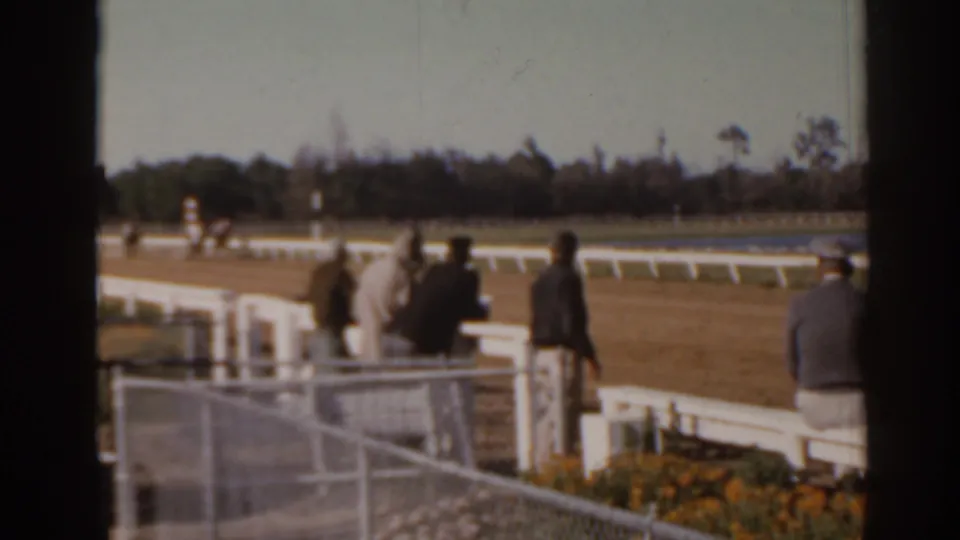 A 1962 Florida racetrack view shows adults near the rail, fencing in the foreground, and horses faintly visible down the track.