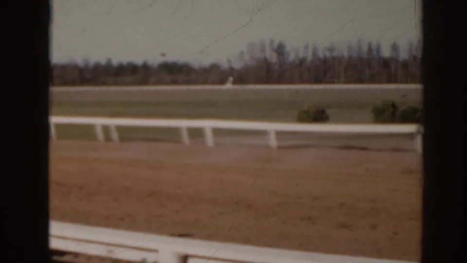 Florida 1962 home-movie frame showing a dirt racetrack, white rail, and distant trees with no close people visible.