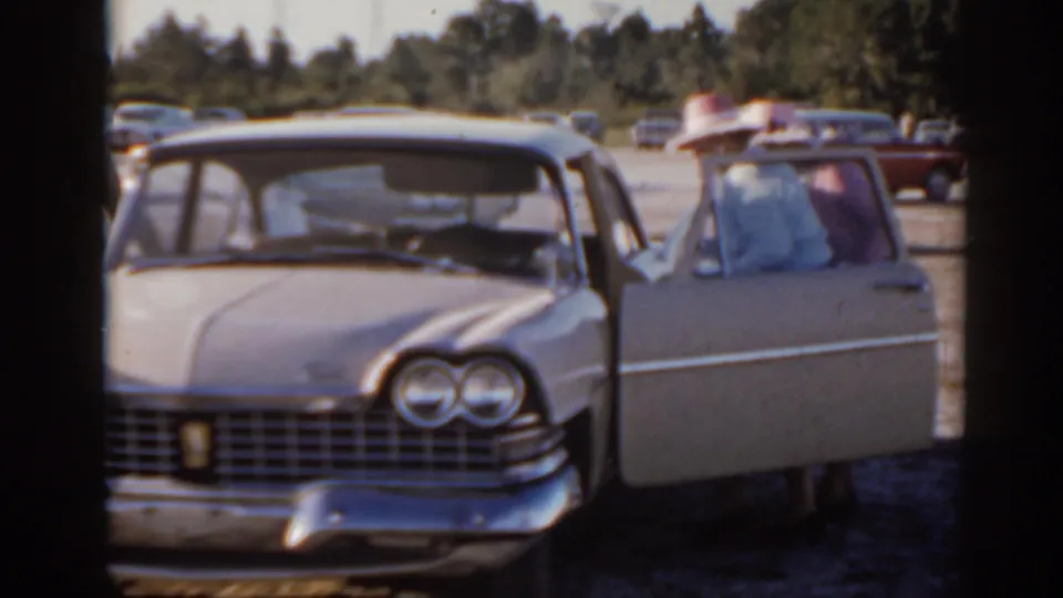 Florida 1962 home-movie view of a light-colored sedan facing camera, with an open door and an adult wearing a wide-brimmed hat.