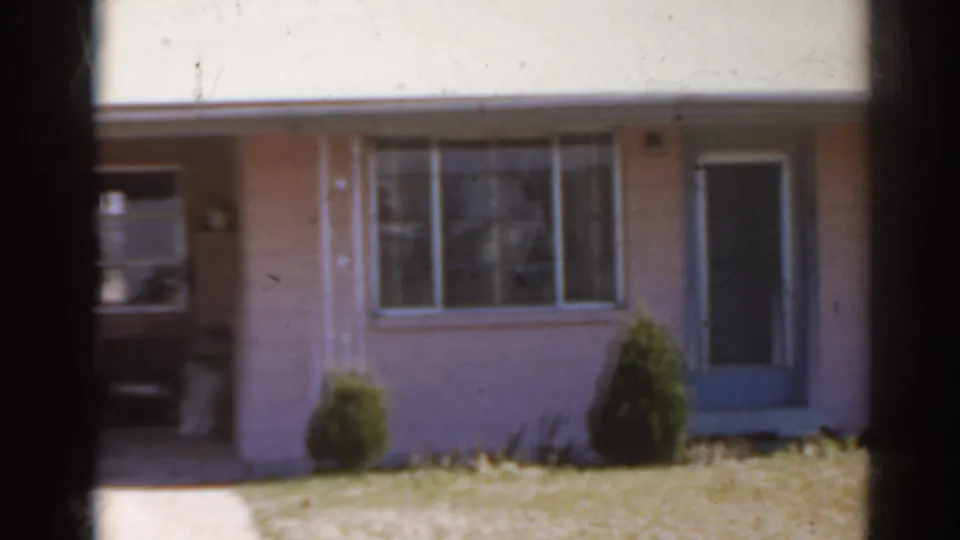 The 1962 home-movie view settles on the pink Florida house facade, blue door, front window, shrubs, and lawn.
