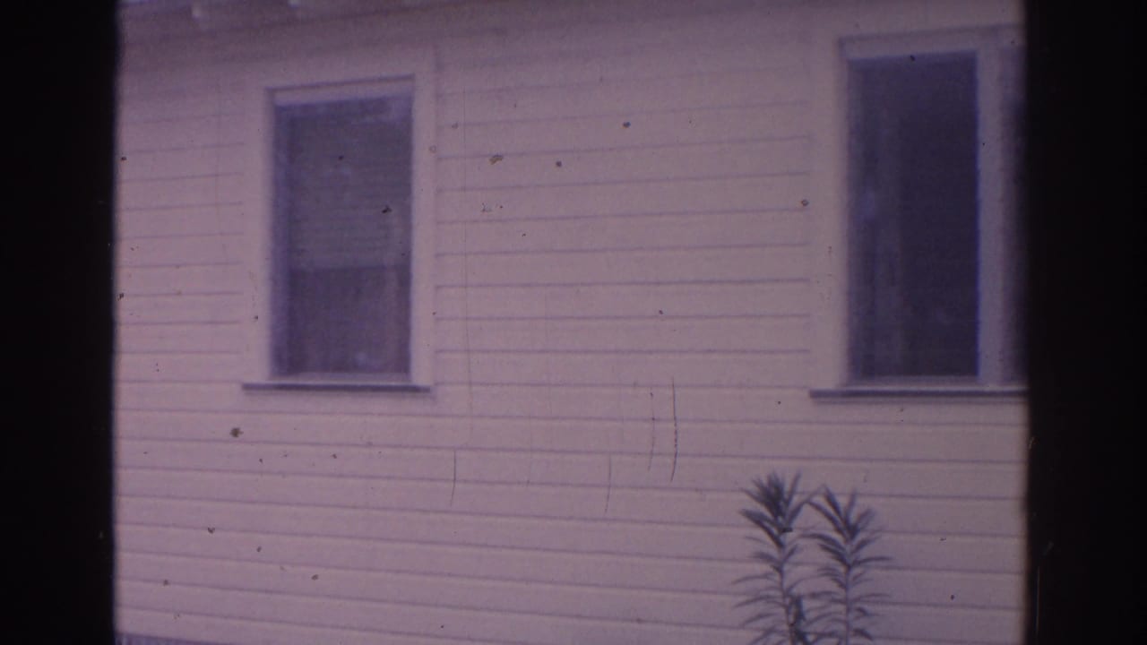 1962 Florida 8mm frame showing a white clapboard house facade with two dark windows and a small plant near the foundation.