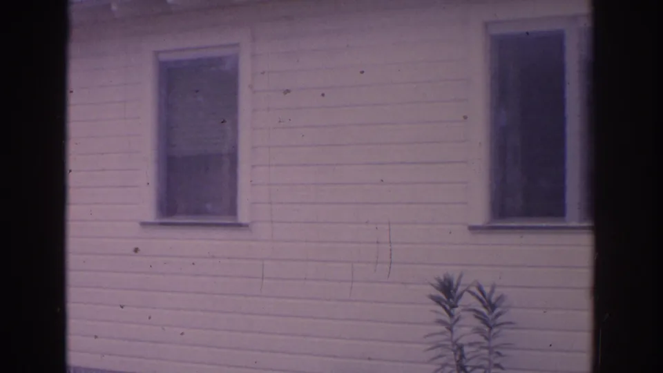 1962 Florida 8mm frame showing a white clapboard house facade with two dark windows and a small plant near the foundation.