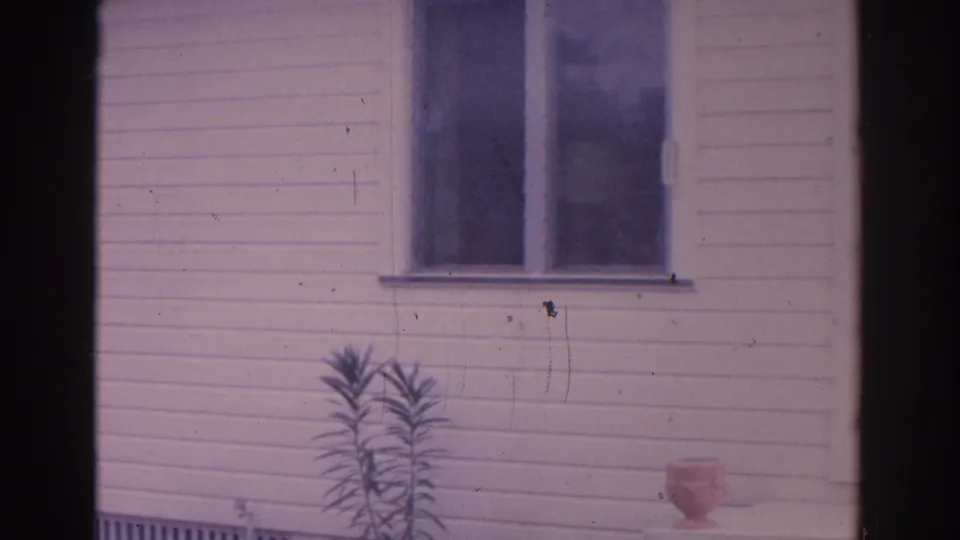 1962 Florida 8mm view of white clapboard siding with paired windows, a small plant, and soft shadows across the facade.