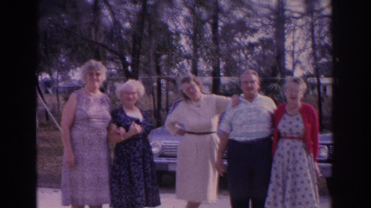 A group of adults faces the camera beside a parked sedan under trees.