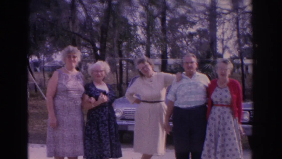 Five adults in dresses and collared shirts face the camera near a mid-century sedan in Florida, supported by the clip metadata.