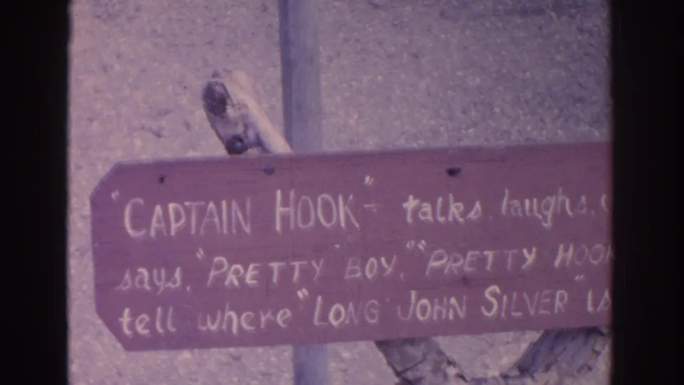 Close 1962 Florida home-movie view of a handwritten themed sign, partly cropped, mentioning Captain Hook and Long John Silver.