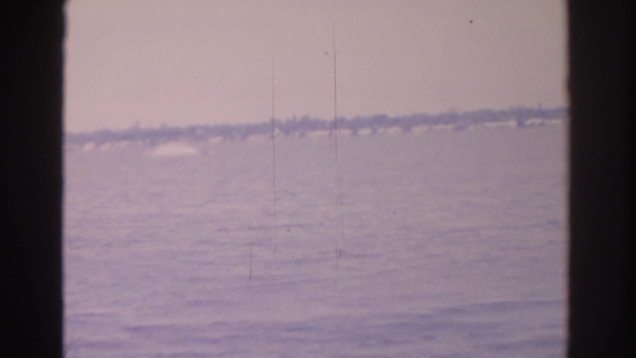 Distant waterfront with open water, low shoreline, and dark 8mm frame borders.