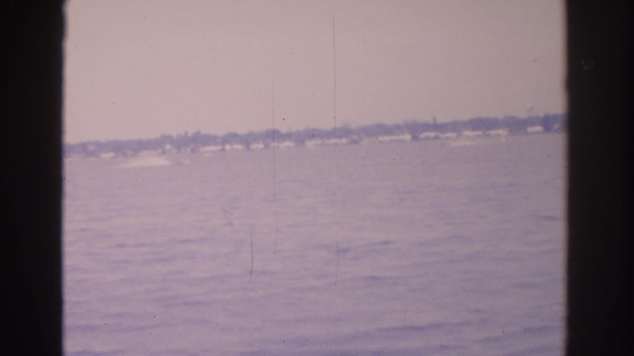 Open water with faint white wake near a distant shoreline under hazy sky.
