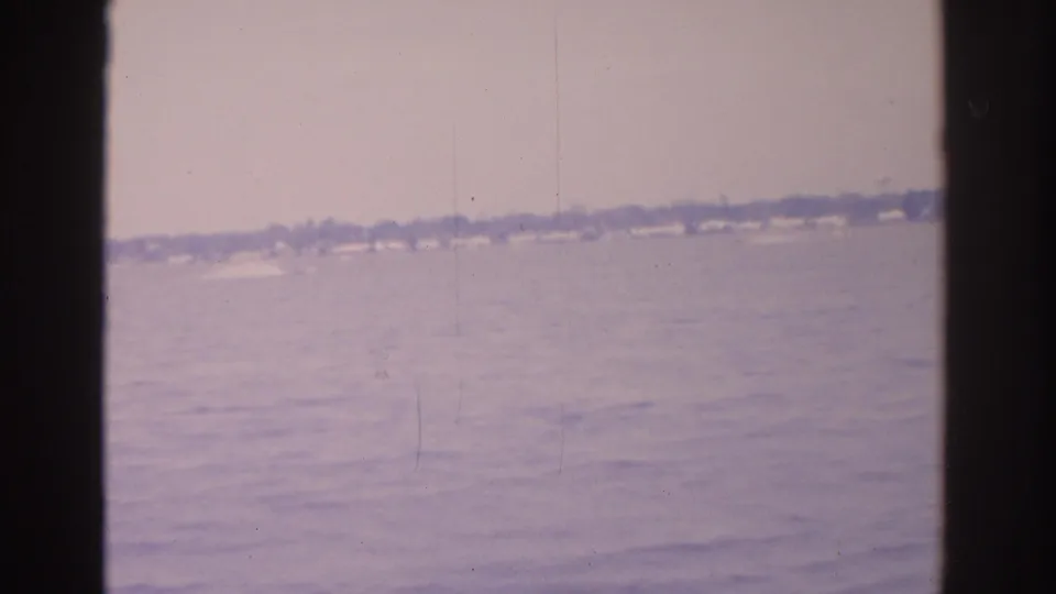 1962 Florida waterfront view with faint speedboat wake on open water and a low distant shoreline.