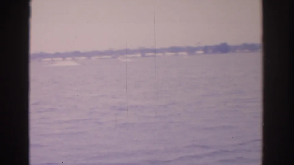 Faded 1962 Florida home-movie frame with open water, distant shore, and a pale wake from a small boat.