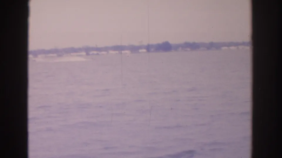 1962 Florida waterfront frame showing calm water, faint wake lines, low shore, and visible 8mm film wear.