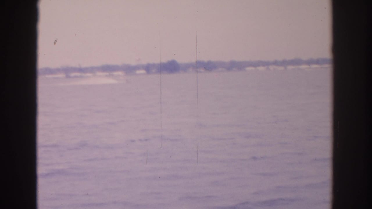 1962 Florida 8mm view across calm water toward a distant shoreline, framed by dark boat-window edges.