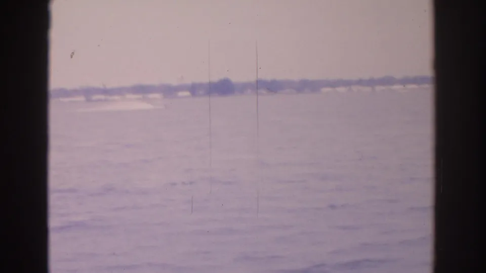 1962 Florida 8mm view across calm water toward a distant shoreline, framed by dark boat-window edges.