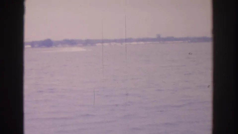 A muted 1962 Florida water view with a far tree-lined shore and dark vertical edges from the filming position.