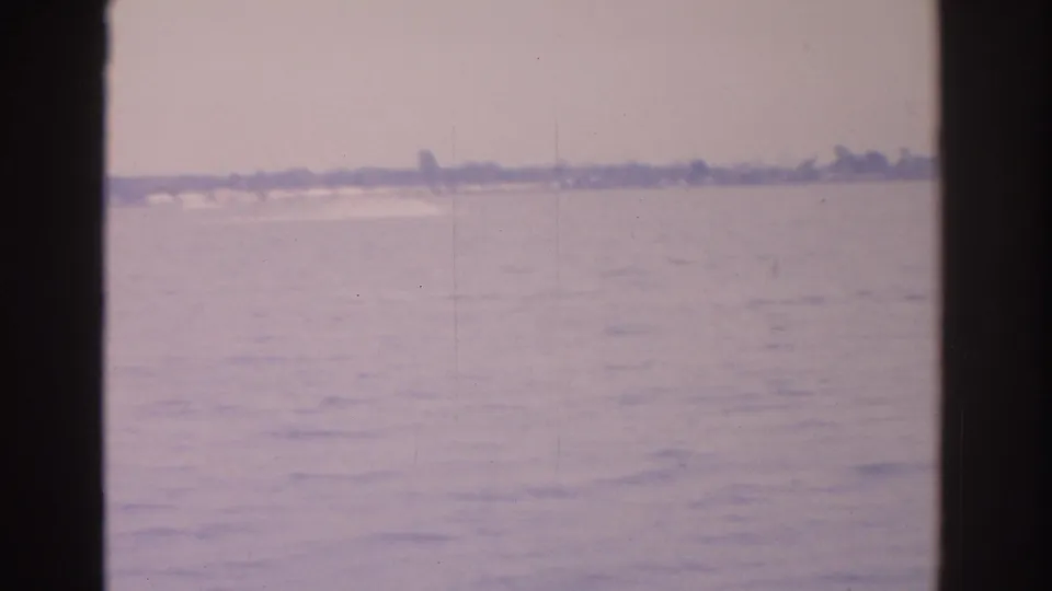 Soft 8mm footage shows Florida water and a low distant shore, with dark framing suggesting filming from inside a vessel.