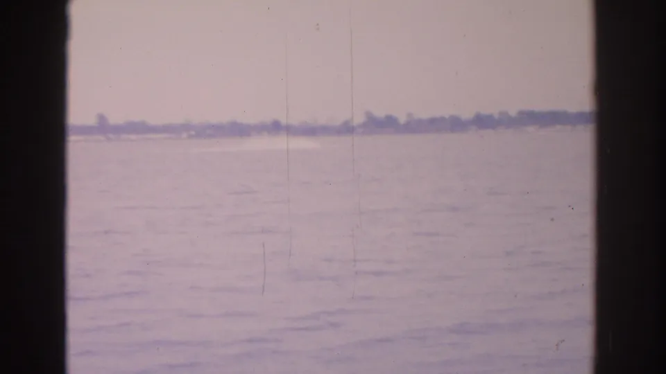 Final 1962 Florida frame holds on calm water, a far low shoreline, dark borders, and visible 8mm film scratches.