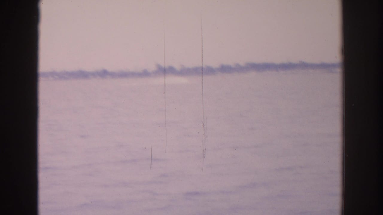 Hazy water surface with a faint distant shoreline and dark film-frame borders.