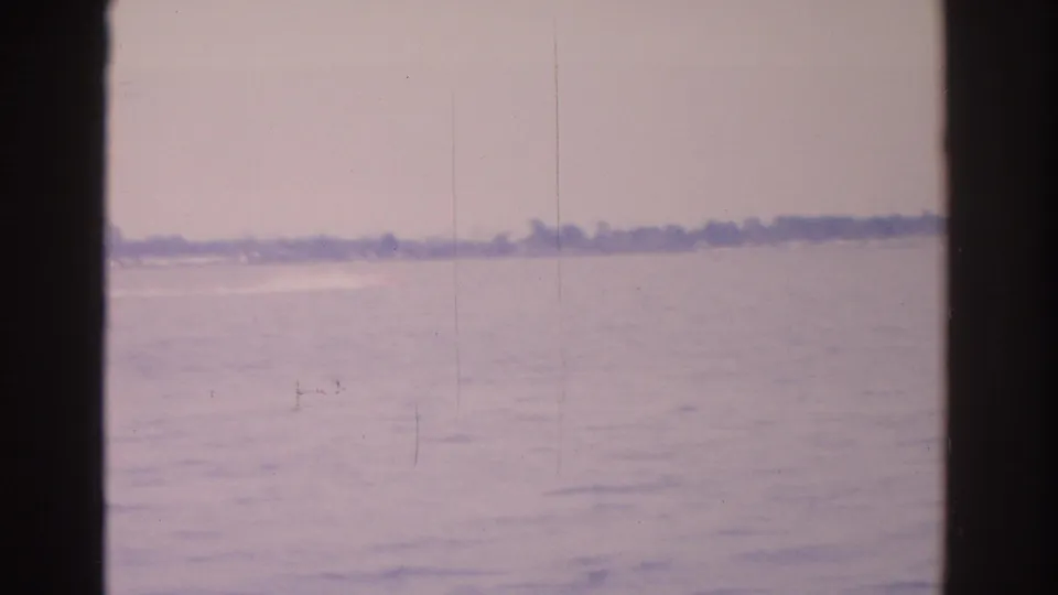 1962 Florida home-movie frame with open water, a faint shoreline, pale sky, and visible 8mm gate borders.