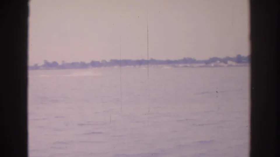 1962 Florida waterfront frame showing rippling water, a low tree-lined horizon, and soft home-movie exposure.