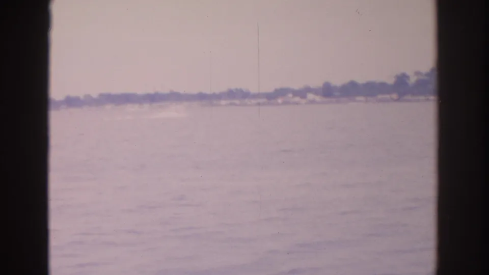 1962 Florida 8mm frame with hazy water, distant shoreline, and a small bright wake or fast-moving object near the horizon.