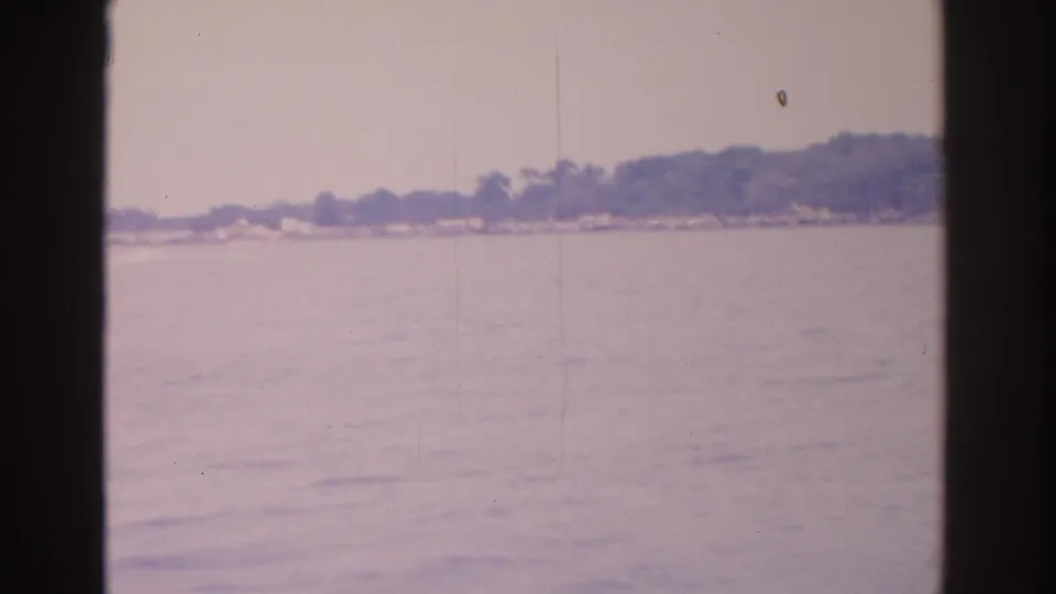 The pan continues across calm water toward a tree-lined Florida shoreline, seen through heavy 8mm frame borders.