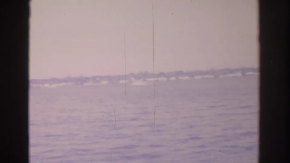 The final 8mm frame looks across calm Florida water toward a faint shoreline with small boats or structures near the horizon.