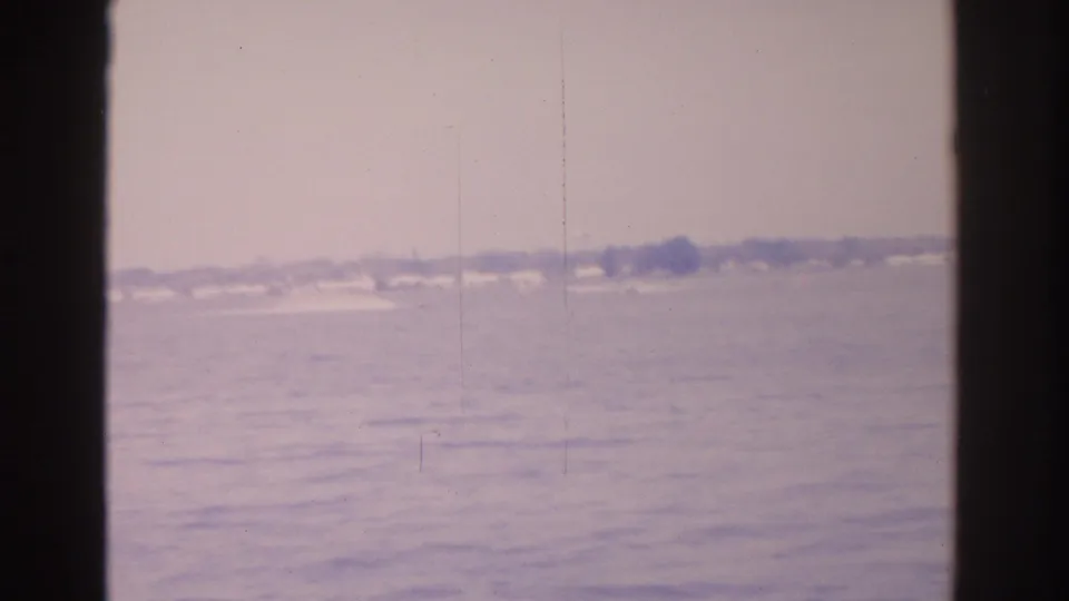 1962 Florida coastal view with distant homes and trees across rippled water, softened by faded home-movie color.