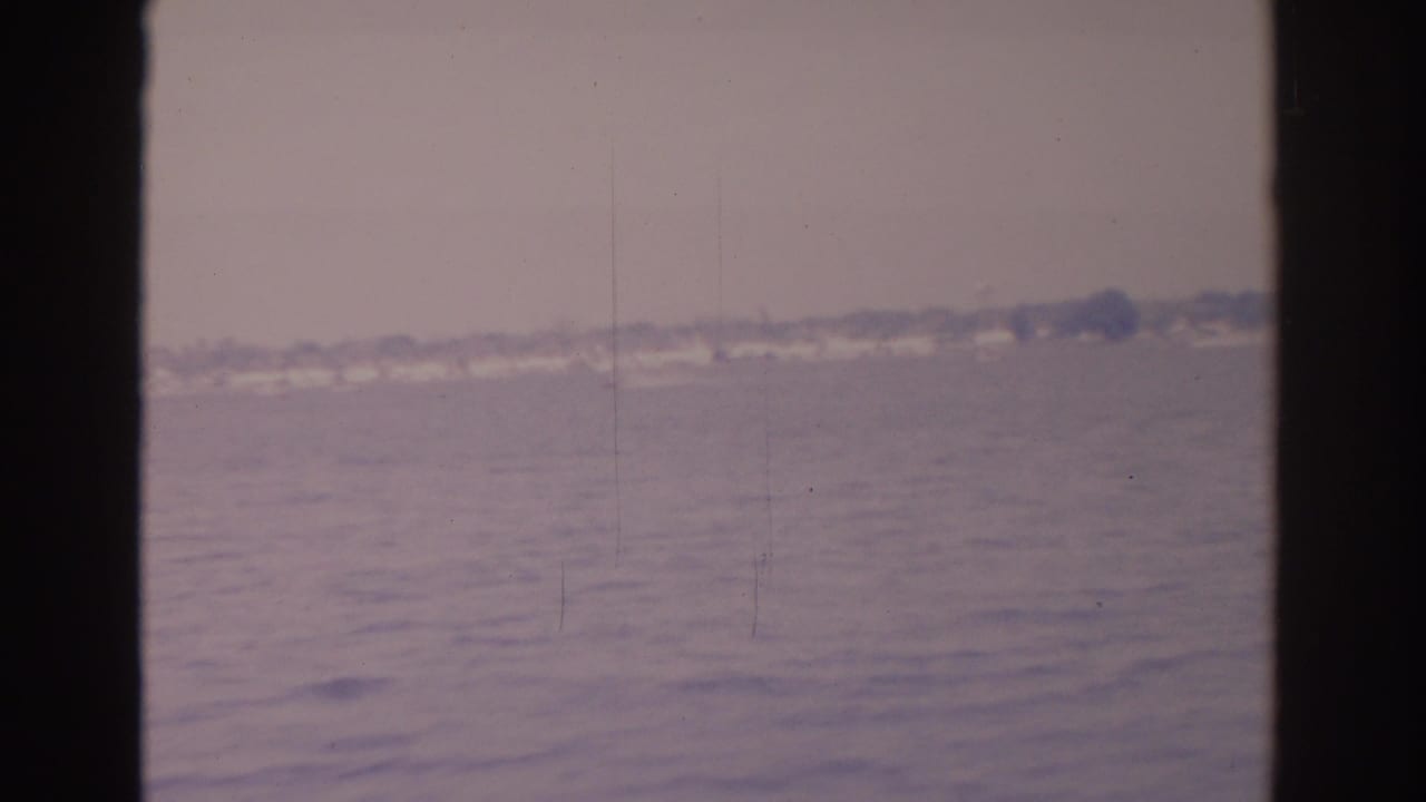 Hazy water and distant shoreline framed by a central dark film divider.