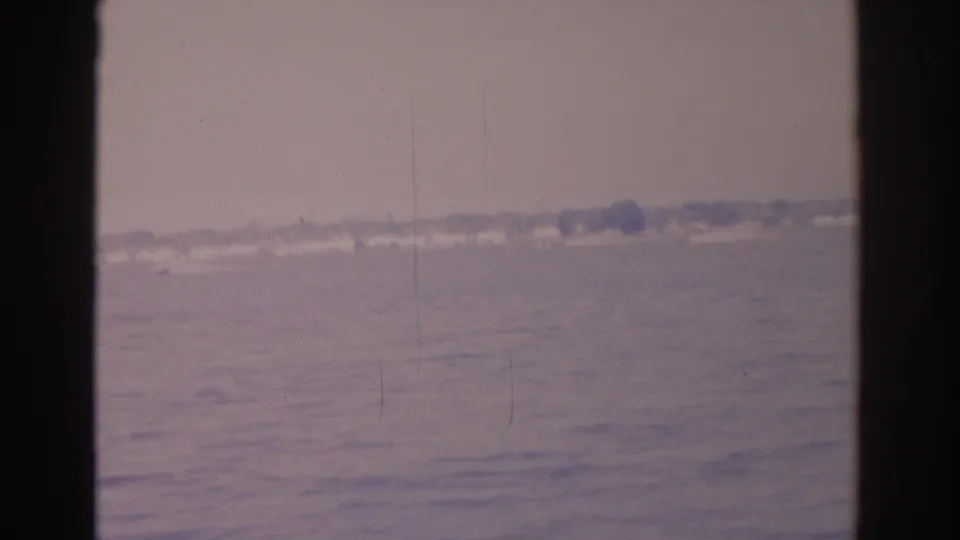 1962 Florida bay footage with muted water, a far low shoreline, possible small boat wake, scratches, and faded home-movie color.