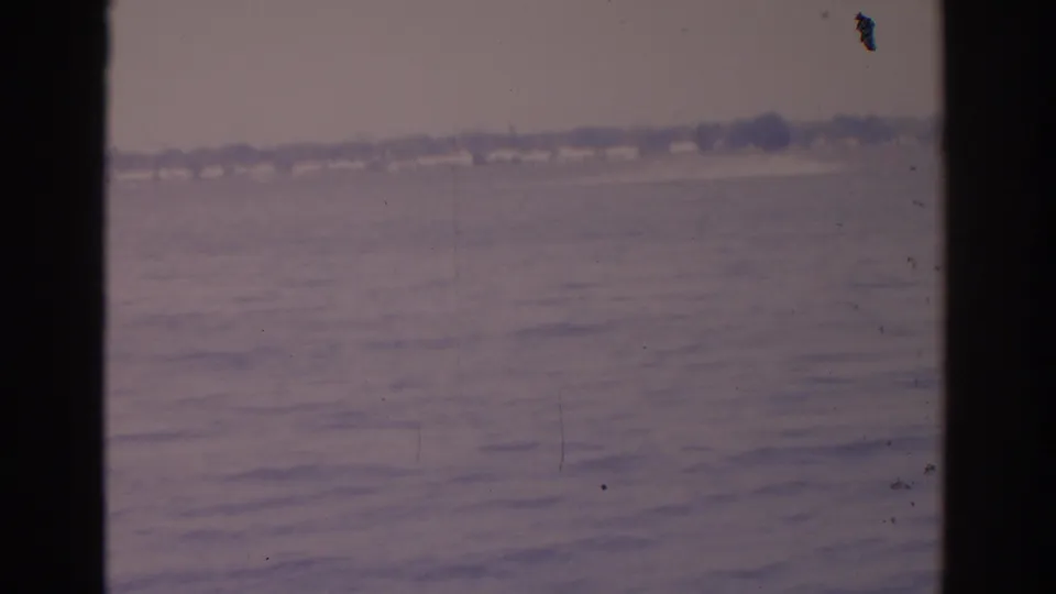 1962 Florida 8mm frame showing open water and a soft distant shoreline under a muted cloudy sky, framed by dark vertical edges.