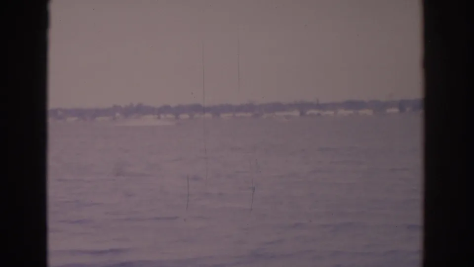 Florida coastal water and a low, indistinct shoreline appear in a muted 1962 8mm frame with dark framing at the sides.