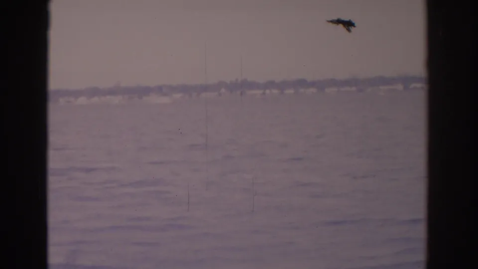 1962 Florida 8mm frame showing calm water from a vessel or window, with a hazy shoreline and a small dark speck above the horizon.