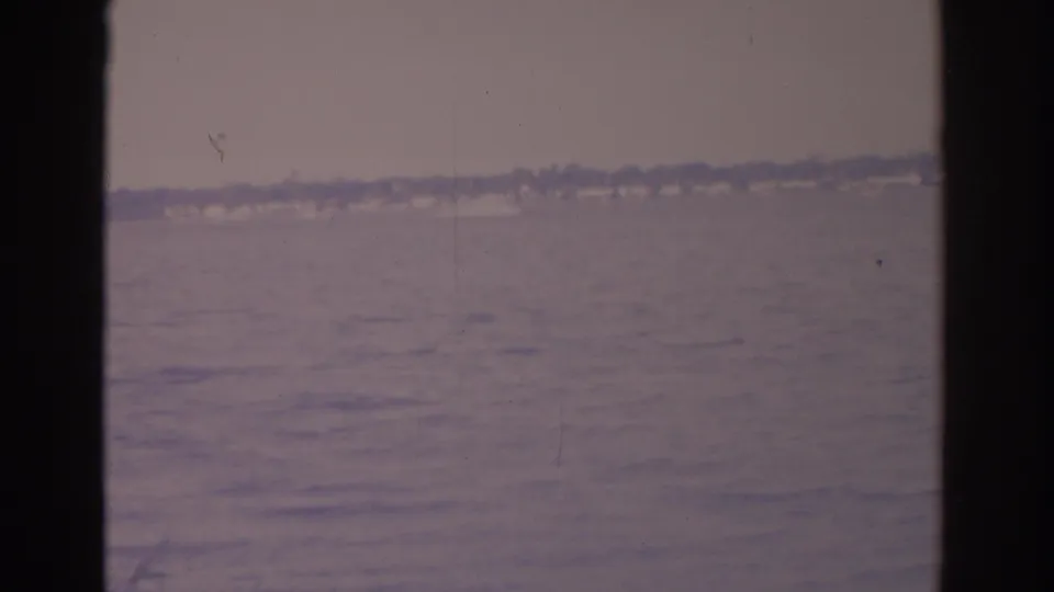 1962 Florida 8mm view across calm water toward a hazy shoreline, framed by dark window or boat-edge bands.